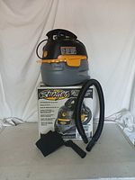 Stinger 2.5 gallon wet/dry vacuum sitting on its original box with accessories including a hose and nozzle attachments displayed in front.