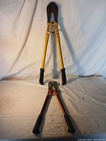 Both bolt cutters placed on a white cloth backdrop, showing full view of each tool with handles outstretched.