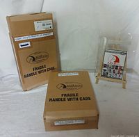 Two sealed boxes labeled with 'Fragile Handle With Care' containing the clear acrylic frames with magnets, showing the quantity label 'clear acrylic frames w magnets x 10 per box'.