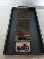Stack of Harley Davidson collector cards in a black tray, showing a card with a red motorcycle