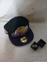 Black and purple Los Angeles Lakers fitted cap with size 7 sticker and box containing #24 pendant