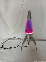 Rocket shaped lava lamp plugged in showing pinkish purple lava inside blue liquid and silver metallic base and top.