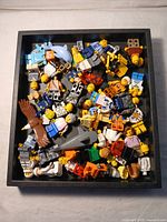 Top view of assorted LEGO figures and parts in a black tray, showing various minifigure bodies, heads, and animal figures.