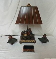 Full view of the lamp with brown shade featuring three monkeys around a globe on the base, two monkey figurine leaf trays on either side, and small rectangular box in front.
