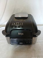 Front view of closed Ninja air fryer showing control panel and lid with handle.
