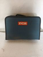 Closed blue and black Ryobi carrying case with red and white logo on front