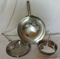 Photo showing all three items: two skillets and one lid, arranged standing and lying flat.