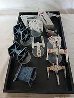 Overview photo of all items arranged in black tray including flight controller box and seven spaceship miniatures.