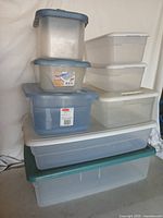 Stack of nine plastic storage containers of various colors and sizes with lids.