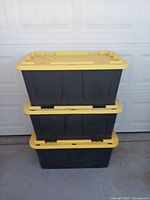 Stacked view of three black Greenmode storage containers with yellow lids.