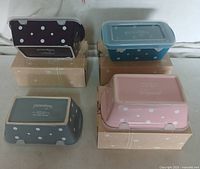 Four Temp-tations by Tara polka dot baking containers placed upside down on respective boxes showing colors and polka dot patterns: dark purple, blue, pink, and gray.