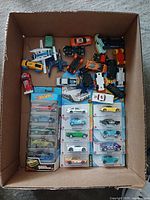 Box of assorted loose die cast cars, toy airplanes, and Hot Wheels cars in packaging