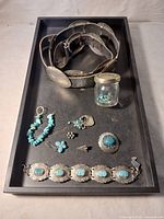 Overview of all items on black tray: belt, jar, earrings, ring/brooch, bracelet