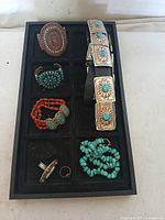 Overall view of display tray showing all jewelry pieces: two cuffs, leather belt, bead bracelets, rings, and necklace.