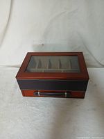 Watch display case closed showing wooden frame, glass lid, and leather handle on front.