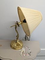 Adjustable brass table lamp with pleated cream fabric lampshade, lamp off, side view showing lamp and shade details.