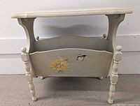 Front and side views of the antique magazine table showing painted floral and butterfly designs and the whimsical curved cutout style.