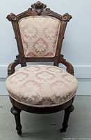 Front view of the full antique Eastlake parlor chair showing round padded seat and detailed wooden legs.