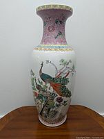 Front view of a tall porcelain vase decorated with peacocks, flowers, and pink patterned border around the neck and base.