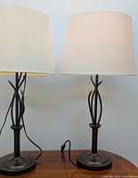 Pair of black metal table lamps with intertwined stems and white shades shown front on.