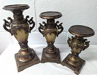 Photo of three ornate candleholders with intricate classical designs, various heights, dark bronze or antique brass finish.
