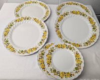 Six white ironstone plates with yellow floral pattern arranged on a white surface showing front pattern and shape.