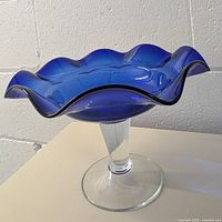 Side view of the cobalt blue glass bowl mounted on a clear glass pedestal, showing scalloped rim and pedestal base.