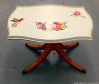 Full view of the side table showing silk cream top with colorful floral and bird painted decorations, and legs with carvings and metal ferrules