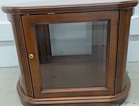 Front view of the wooden display cabinet showing single glass door with brass knob and fluted side details.