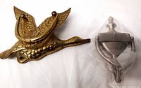 Top view of vintage brass flying goose door knocker and new modern metal door knocker still sealed in plastic.