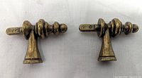Close-up photo of two antique brass finish cabinet/dresser knobs with turned spindle design, showing detail and structure.