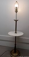 Full view of the brass floor lamp with attached white marble table under the light bulb without a lampshade, showing the tall central column and the brass base on the floor.