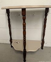Front angle showing the half moon table with dark wood turned spindle legs and cream painted top and bottom shelves with decorative motifs.