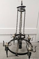 Full view of medieval style iron chandelier suspended by chains showing 4 torch style lights around outer circle and one central light