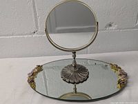 Photo of the round standing mirror with a gold frame and metal decorative base placed on the mirrored tray.