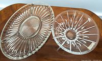 Two Nachtmann clear glass pieces, showing a divided oval serving dish with intricate cut pattern and a round decorative bowl with starburst cut design, both placed on a wooden surface.