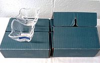 Two unopened green boxes labeled Villeroy & Boch with one clear square wave glass sauce dish placed on top of the boxes, showing the shape and size.