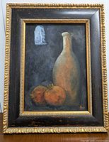 Frontal photo of the oil painting showing a tall light bottle and two orange pomegranates on a dark background, framed in a black and gold wooden frame.