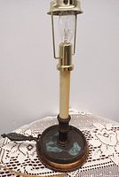 Rustic cast iron chamber candlestick lamp standing unlit on a crocheted lace table cover showing patina on the base and brass fittings.