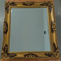 Front view of the ornate rectangular mirror showing the detailed golden wooden frame with dark brown accents and beveled mirror glass.
