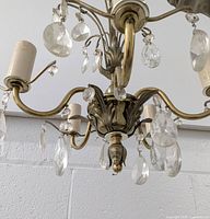 Close-up showing metal arms, light sockets with candle-style sleeves, and hanging crystal prisms