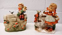 Front view showing two ceramic planters with children and bird figurines, highlighting colors and details.