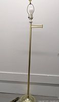 Tall brass floor lamp with adjustable swivel arm and round base, shown unlit.