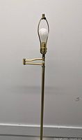 Brass adjustable swivel floor lamp standing unlit showing harp bulb holder and weighted round base with patina and some scratches.