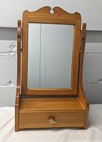 Front view of the vintage wooden swivel tabletop mirror with drawer, showing the full mirror surface and drawer front with knob.