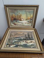 Both winter landscape oil paintings by A. Kalvans, matted and framed, showing snowy outdoor scenes with trees and hills.