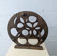 Photo showing front view of vintage wooden wheel wine holder with a dark wood finish and multiple circular slots for wine bottles.