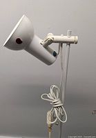 Close-up photo of the white lamp head showing the hinge and adjustment knob, cord wrapped around the stand, and inline switch on the power cord.