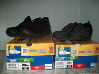 Two pairs of black women's Skechers slip-in sneakers displayed on boxes labeled with size 8, wide fit, memory foam, machine washable, and vegan friendly.