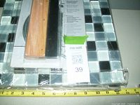 Close-up of a tile tool kit with wooden and metal tools on top of glass tile sheets, all new and still in plastic wrapping.